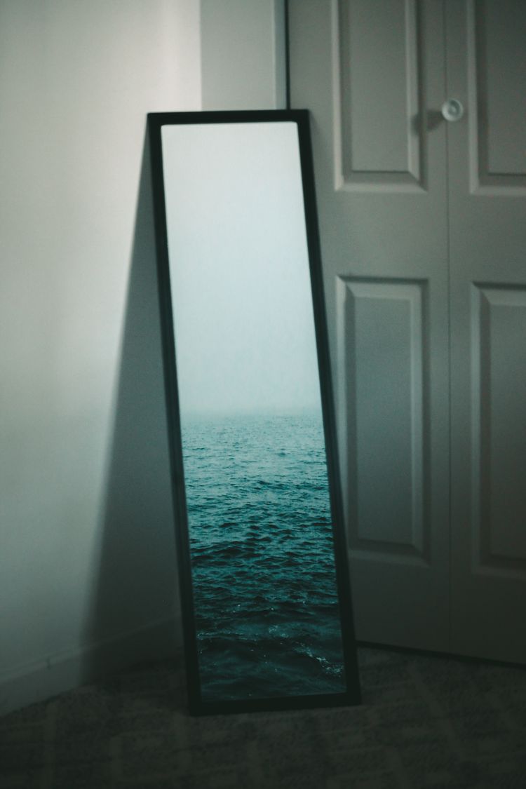 A surreal picture of a mirror in the corner of a room reflecting ocean waves